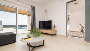 A modern living room with a flat-screen TV, a round coffee table, and a potted plant. - South Beach Villas - 2 bedroom sea view with heated pool (Γεννάδι)