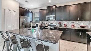 Eine moderne Küche mit dunklen Schränken, Granit-Arbeitsplatten, einem Edelstahl-Kühlschrank, einer Mikrowelle und einer Kaffeemaschine.