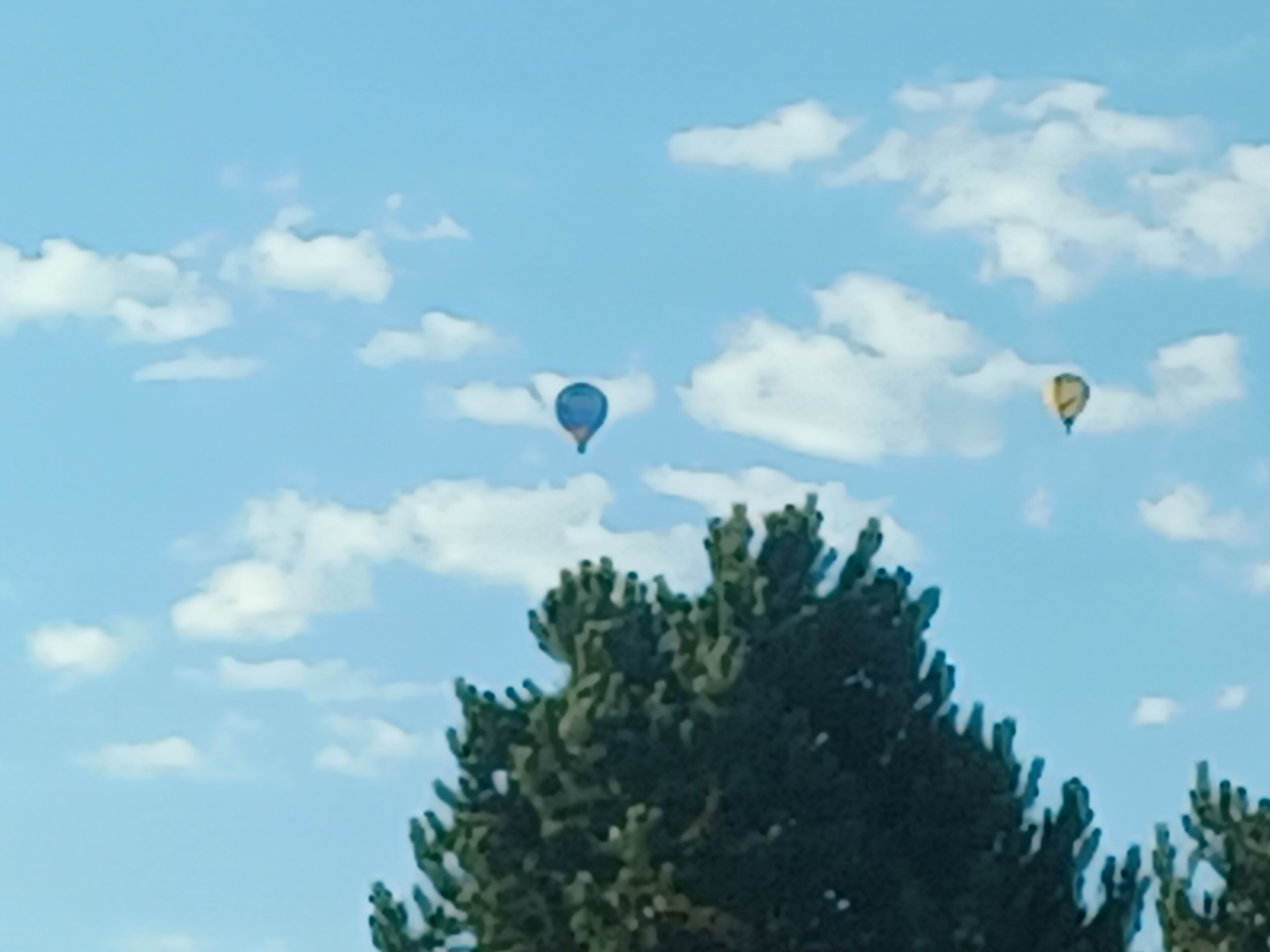 Three hot air balloons in a clear sky with some clouds.