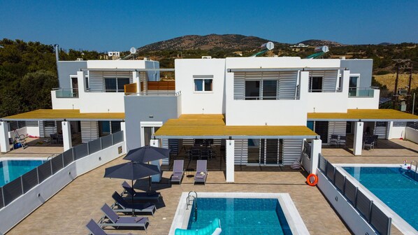 Un hotel moderno con dos piscinas, zona de estar al aire libre y vistas a las colinas.
