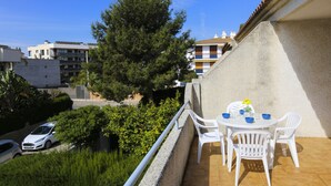 A balcony with a table and chairs, a car parked below, and buildings in the background.