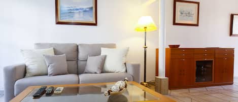 A living room with a sofa, a glass coffee table, a lamp, and a cabinet.
