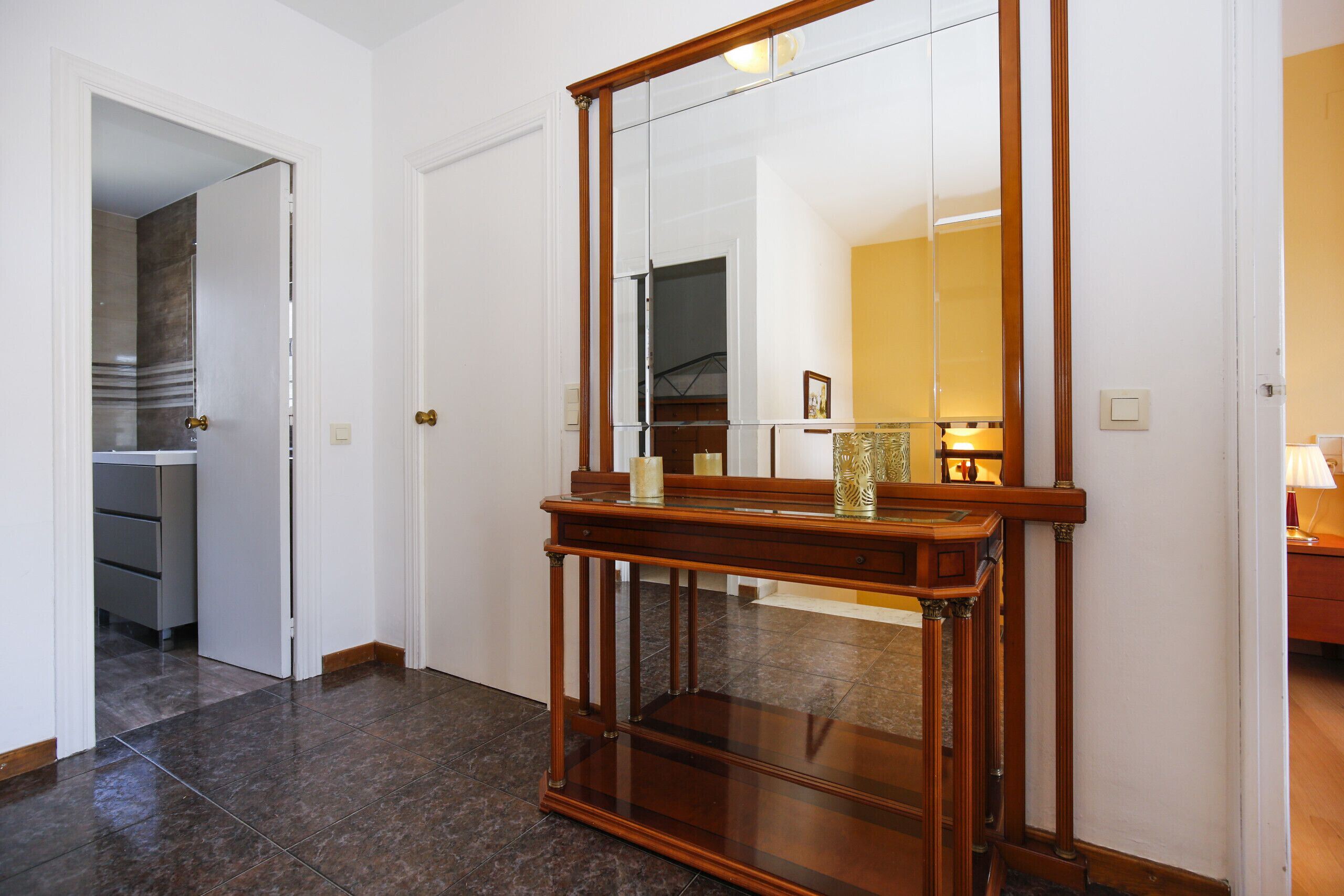 Een hal met een houten console tafel en een grote spiegel. Een deur leidt naar een keuken.