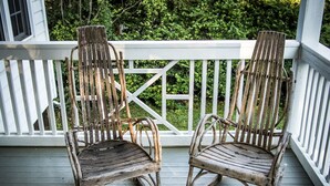 Deux fauteuils à bascule en bois rustique, placés sur une terrasse en bois dotée de rampes blanches.