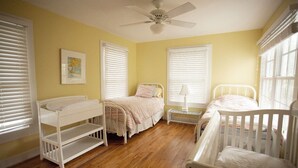 Une chambre d’enfant avec un lit superposé, un berceau, une table de chevet et un ventilateur de plafond.