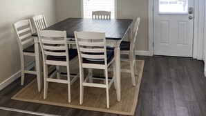 A dining area with a dark wooden table and white chairs, a small rug, and a door with a window. - Ly'an High Lodge - Venice Marina (Venice)