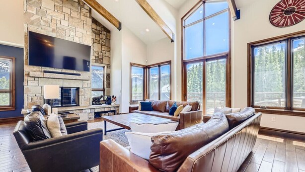 A spacious living room with a stone fireplace, leather sofas, and large windows offering a view of the outdoors.