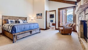 A bedroom with a wooden bed, a leather chair, a stone fireplace, and a view of the outdoors.