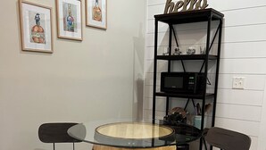 Een houten tafeltje met twee stoelen, een metalen wandplank zwart van kleur met een 'hello'-bordje, en ingelijste foto's aan de muur.