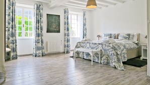 A bedroom with a bed, a bench, a radiator, and a window with curtains.