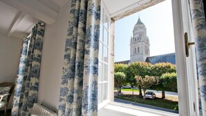 A room with a window overlooking a church tower and a street view.