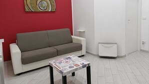 Un salon avec un mur rouge, un canapé gris, une table basse ornée d’un motif d’imprimé de journal et une porte blanche.