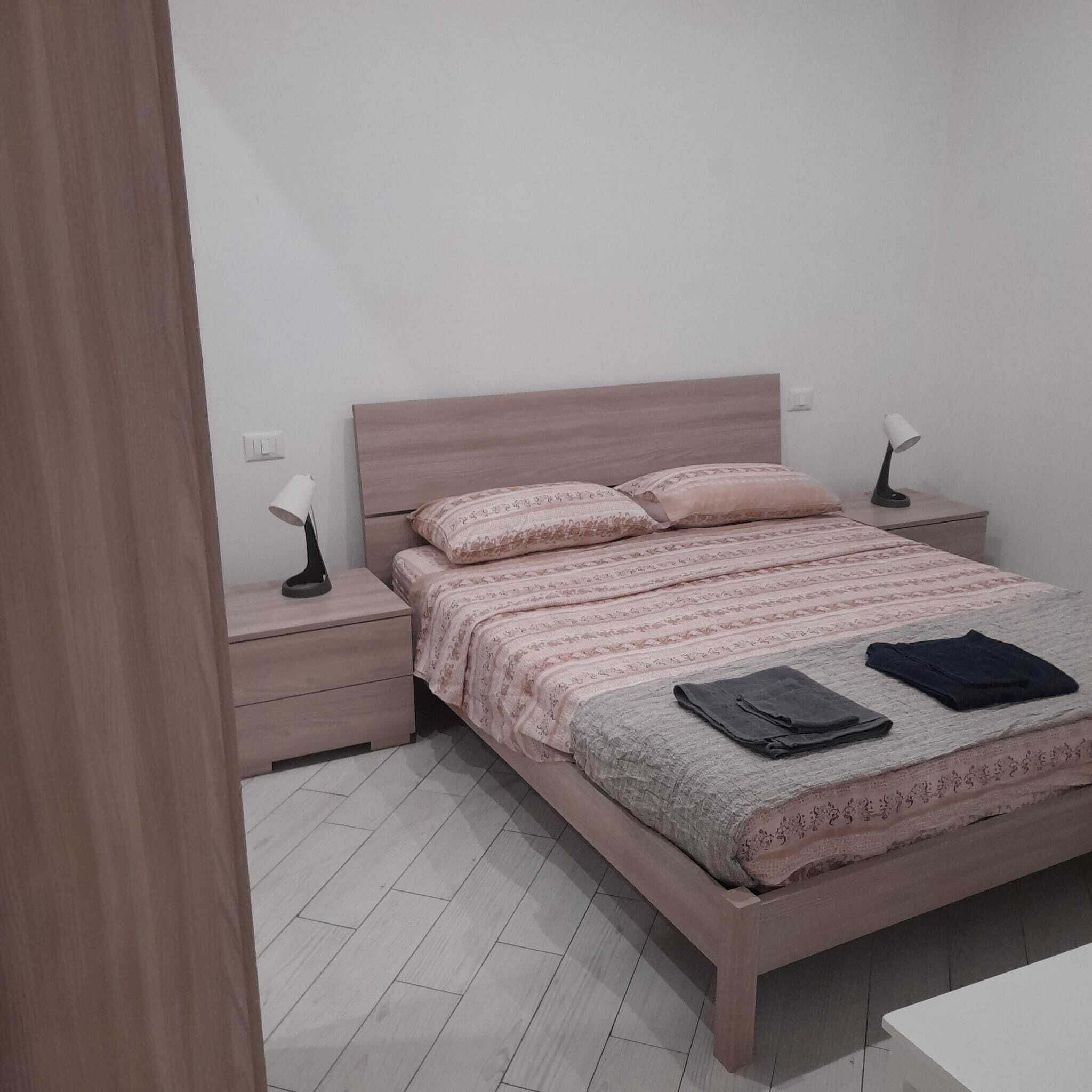 Un dormitorio con una cama de madera, dos mesitas de noche, una lámpara en cada una y una mesita de noche blanca.