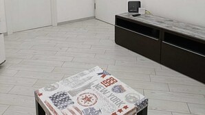 Une pièce aux murs blancs, avec un sol carrelé, un bureau avec un ordinateur, un téléviseur à écran plat et une porte dotée d’un téléphone.