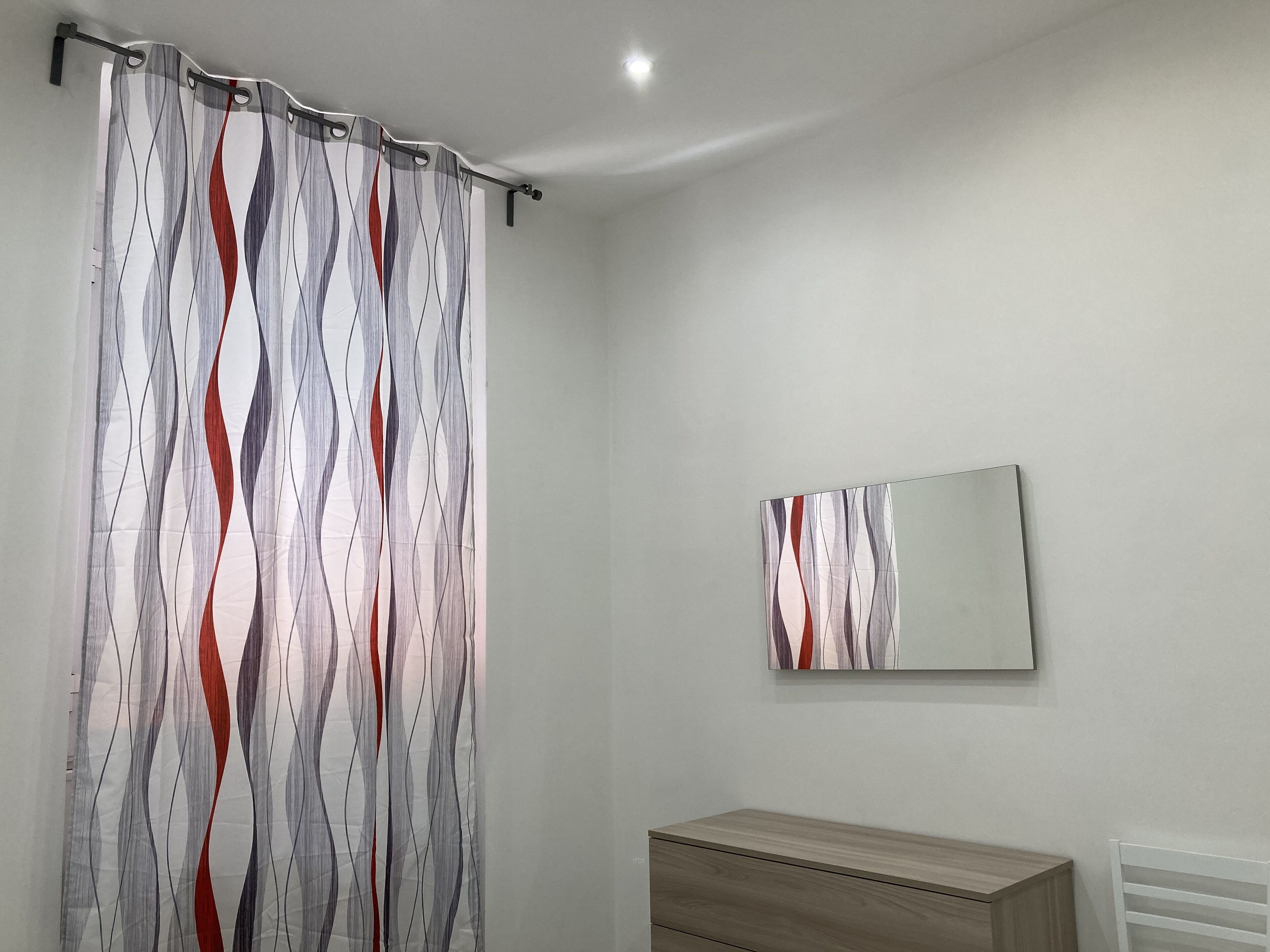 Une salle de bain avec un rideau de douche, un miroir et une commode en bois.