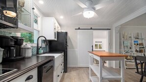 A modern kitchen with a black refrigerator, white cabinets, and a wooden table. - New Remodel! Updated Cottage near Beach and Park (Manistee)