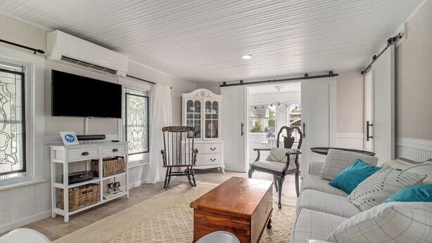 A living room with a television, white furniture, a wooden coffee table, and a white sofa with blue cushions. - New Remodel! Updated Cottage near Beach and Park (Manistee)