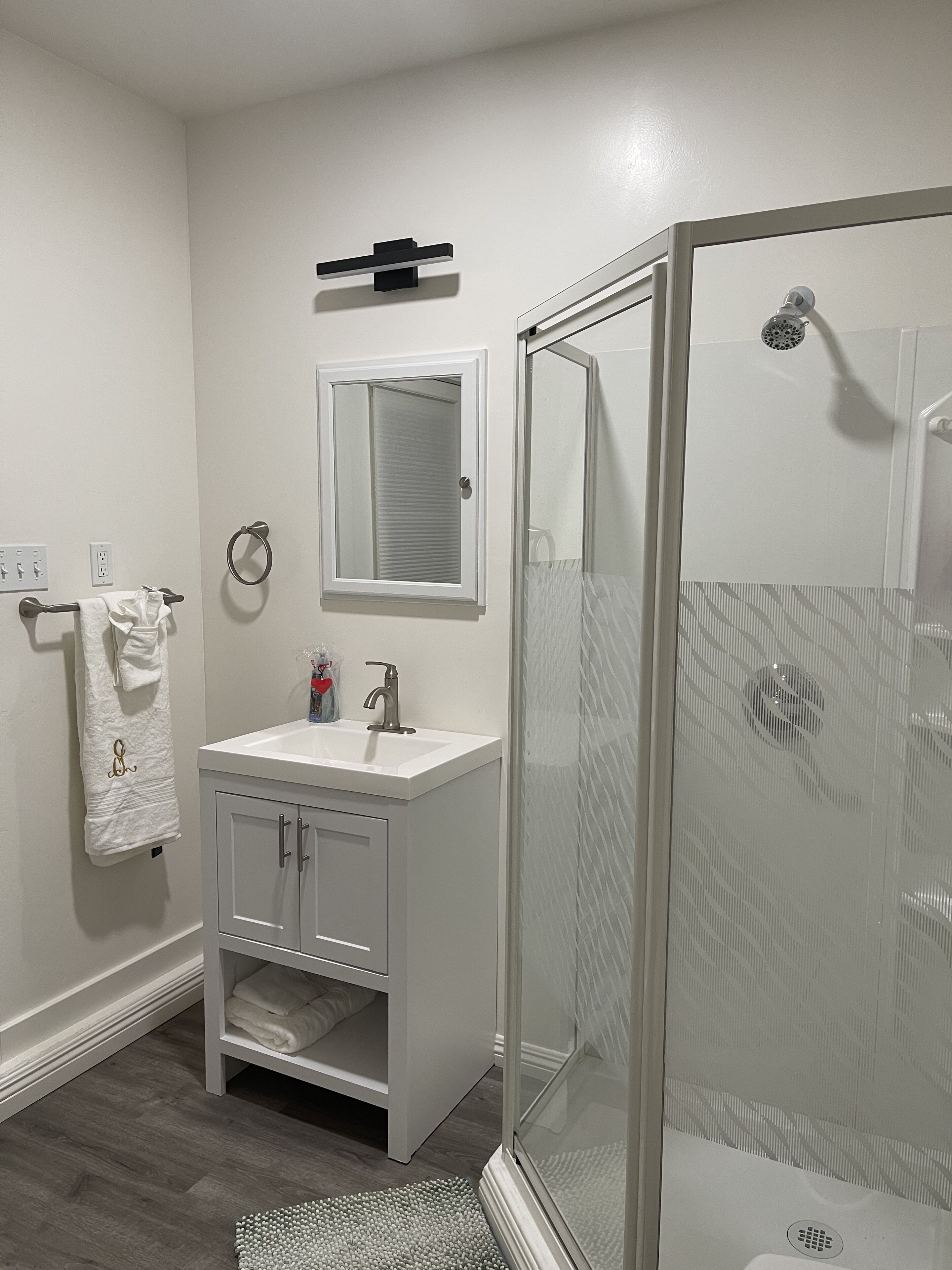 Une salle de bain avec un meuble-lavabo blanc, une cabine de douche en verre et un porte-serviettes.