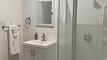 Une salle de bain avec un meuble-lavabo blanc, une cabine de douche en verre et un porte-serviettes.