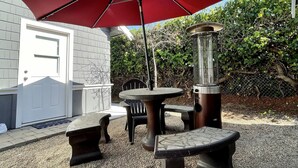 Un patio al aire libre con una sombrilla roja, una mesa redonda, bancos y un farol.