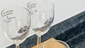 Tres copas de vino sobre una bandeja de madera con texto grabado, colocadas sobre una encimera de cocina.