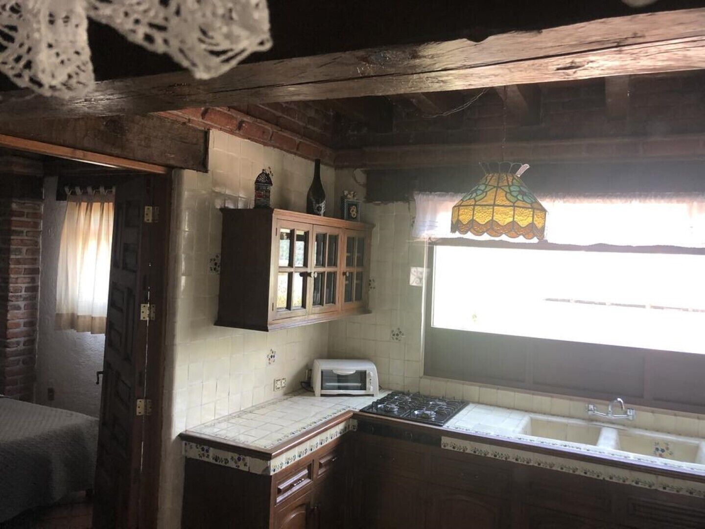 Une cuisine rustique avec un plafond en bois, une fenêtre ornée d’un lampadaire en vitrail, un four encastré et un petit évier.