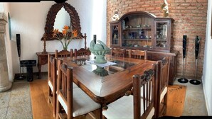 Uma sala de jantar com uma mesa e cadeiras de madeira, um vaso decorativo e uma parede de tijolos com um armário.
