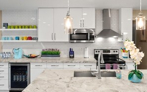 A modern kitchen with white cabinetry, stainless steel appliances, and a marble countertop.