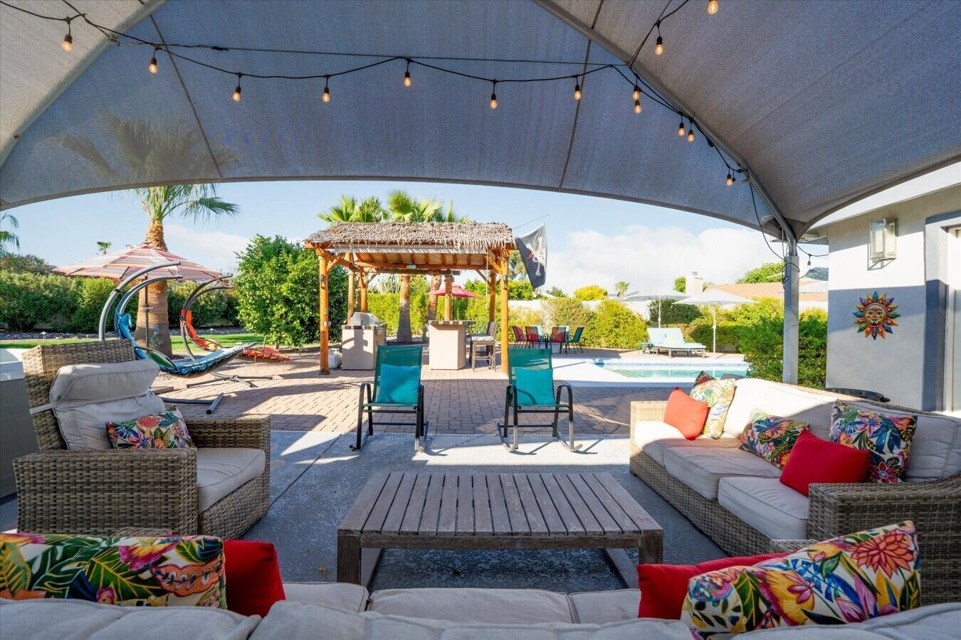 An outdoor patio with wicker furniture, a wooden table, and a pergola with string lights.