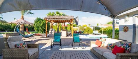 An outdoor patio with wicker furniture, a wooden table, and a pergola with string lights.
