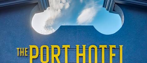 Une enseigne d’hôtel avec le nom « The Port Hotel » écrit en lettres jaunes et en caractères gras sur un fond bleu.