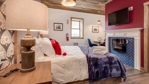 Ett hotellrum med en säng, en lampa, en tv, en öppen spis och ett fönster.