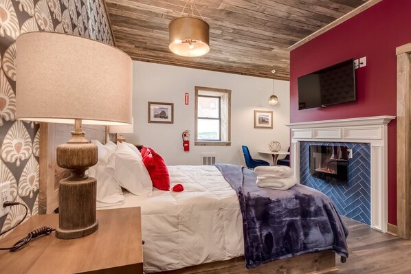 Ein Hotelzimmer mit Bett, Lampe, Fernseher, Kamin und Fenster.