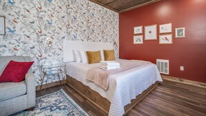 Un dormitorio con techo de madera, cama con cabecera blanca, pared roja con cuadros enmarcados y alfombra estampada.
