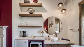 Ein modernes Badezimmer mit integriertem Waschbecken, einem runden Spiegel und einer Kaffeemaschine.