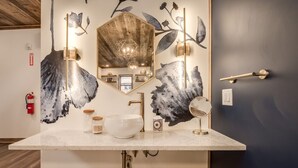 Une salle de bain avec un grand miroir, un lavabo et un mur décoratif orné de motifs de feuilles.