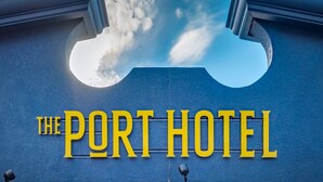 Une enseigne d’hôtel avec le nom « The Port Hotel » écrit en lettres jaunes et en caractères gras sur un fond bleu.
