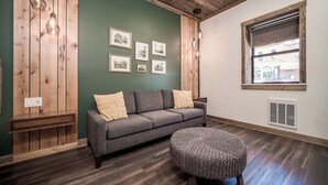 Una sala de estar acogedora con un sofá gris, un otoman tejido redondo, paneles de madera en las paredes y cuadros enmarcados.