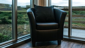 A corner room with large windows, a leather chair, and wooden flooring.