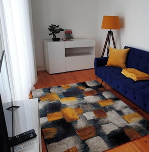 Ein Wohnzimmer mit einer Couch, einer Lampe, einem Fernseher und einem Teppich mit Muster.
