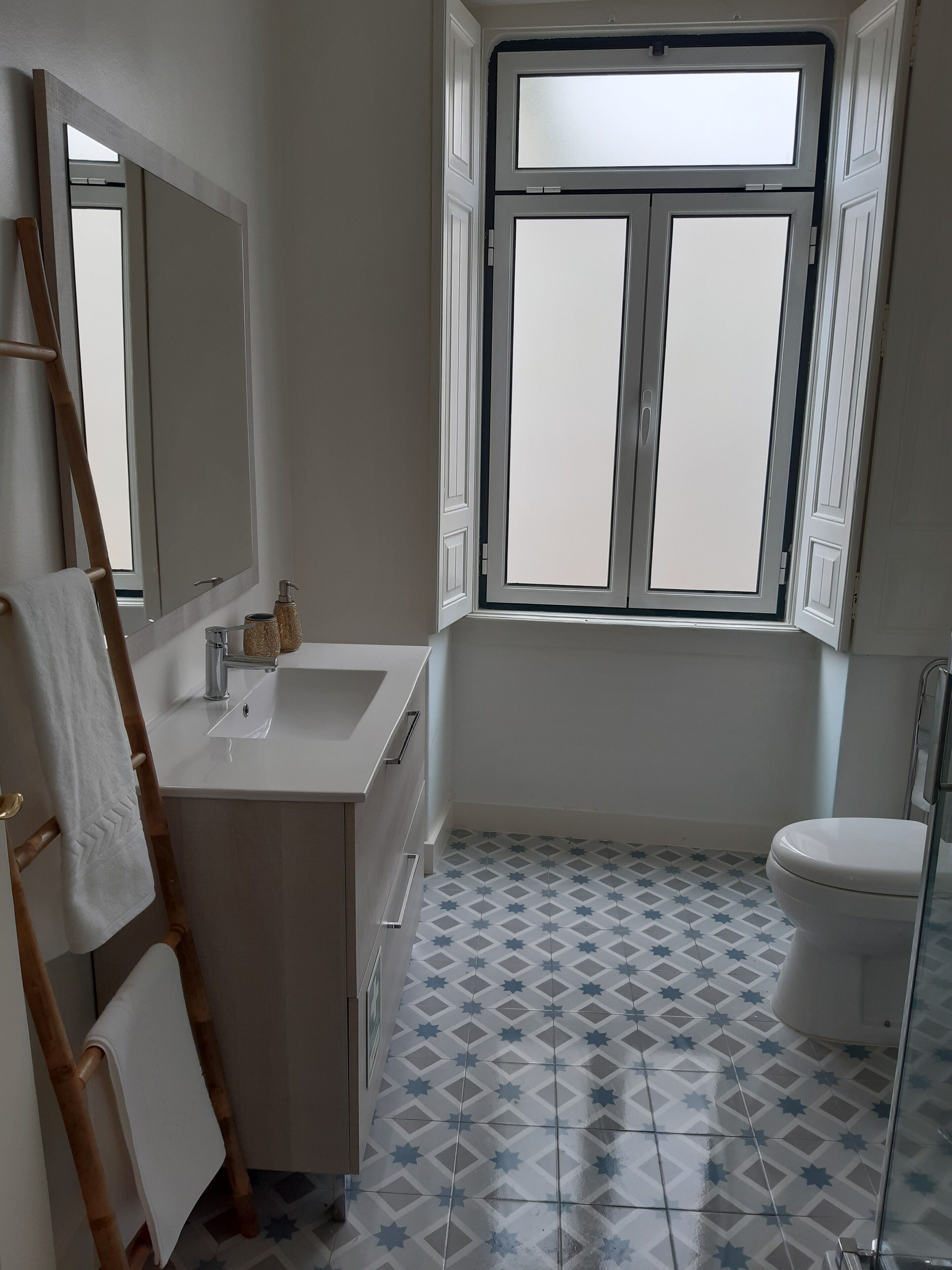Une salle de bain avec un lavabo blanc, des toilettes et une fenêtre aux carreaux de verre dépoli.