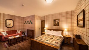 A neatly arranged bedroom with a wooden bed, a red sofa, a small table, and a nightstand with lamps. - The wooden floors, vintage furniture, and tartan accents create a comfy room (Inverness)