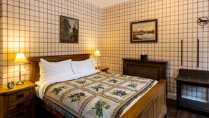 A hotel room with a checkered wall pattern, a wooden bed with a floral bedspread, two bedside lamps, and a nightstand with a clock. - The wooden floors, vintage furniture, and tartan accents create a comfy room (Inverness)