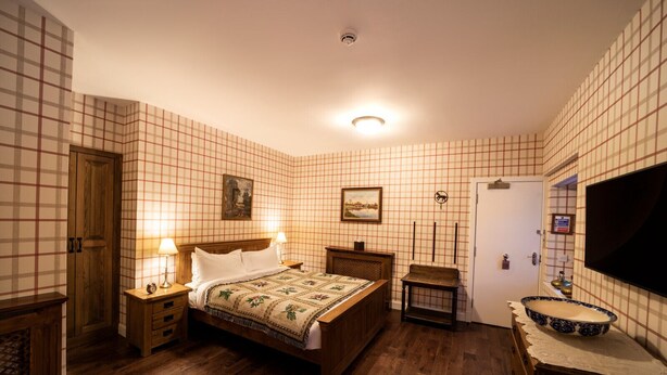 A bedroom with a wooden bed, two bedside tables with lamps, a small bedside table with a clock, a wooden bench, a large mirror, and a television on the wall. - The wooden floors, vintage furniture, and tartan accents create a comfy room (Inverness)