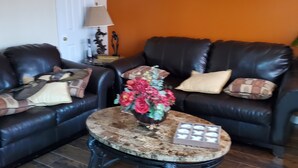 Ein Wohnzimmer mit zwei schwarzen Ledersofas, einem runden Couchtisch mit Blumen und einer Lampe auf einem Beistelltisch.