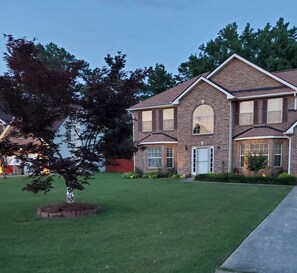 A two-story brick house with a front yard, a tree, and a driveway.