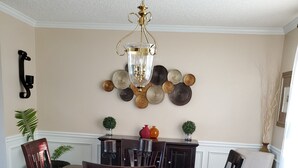 Ein Esszimmer mit großem Holztisch, sechs Stühlen, einer Pendelleuchte, Wanddekoration und einem Blumentopf.