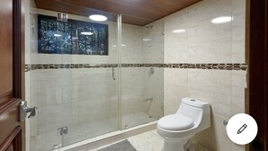 Un baño moderno con ducha de vidrio, inodoro y ventana con vista a árboles.