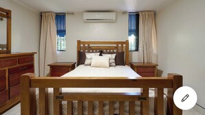 Un dormitorio con una cama de madera, dos mesitas de noche, un aparador y un equipo de aire acondicionado.