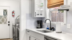 A kitchen with a built-in dishwasher, a coffee maker, and a window with blinds. - Magnolia House- Walkable Uptown, Kids Playhouse, Peaceful Peacocks, Near Beach! (St. Augustine)